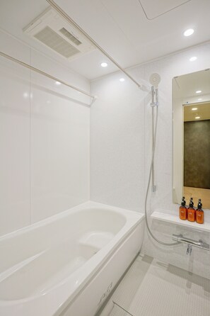 A modern bathroom with a white bathtub, a shower area, and a mirror above the sink. - Dash Living Nezu (Bunkyo-ku)