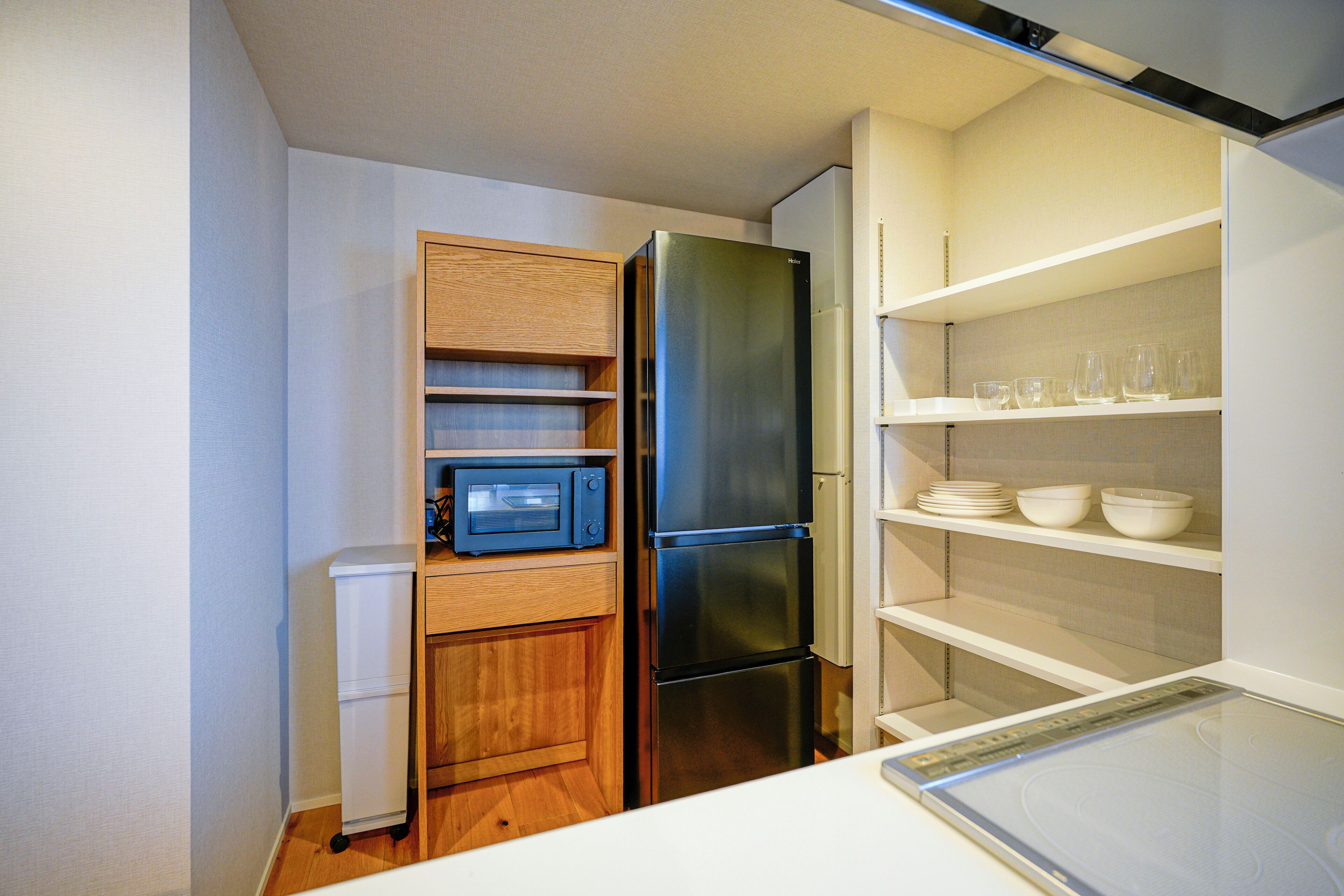 Una cocina compacta con microondas integrado, un refrigerador de acero inoxidable y un estante blanco con tazones y vasos.