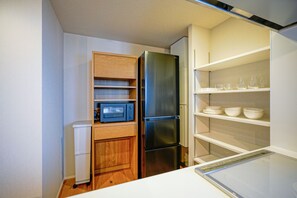 A compact kitchen with a built-in microwave, a stainless steel refrigerator, and a white shelf with bowls and glasses. - Dash Living Nezu (Bunkyo-ku)