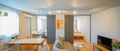 A modern hotel room with a kitchenette, a sofa, a dining table, and a TV.