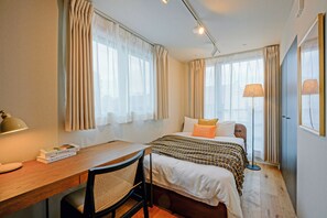 A hotel room with a bed, a desk, a chair, a lamp, and curtains. - Dash Living Nezu (Bunkyo-ku)