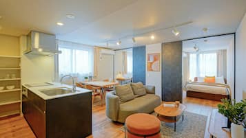 A modern hotel room with a kitchenette, a sofa, a dining area, and a separate bedroom.