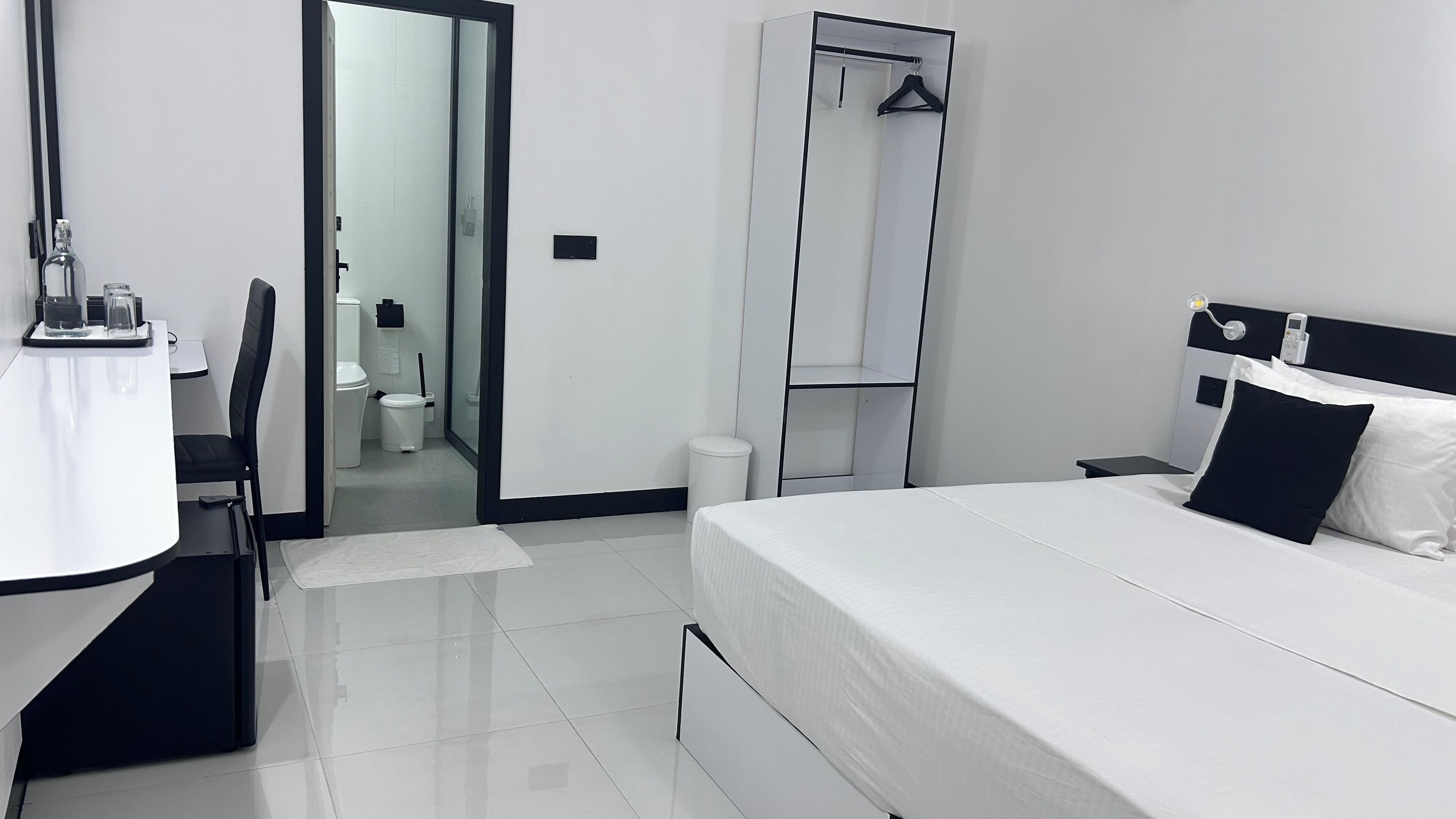Una habitación de hotel con cama, escritorio con silla, espejo, armario y un inodoro.
