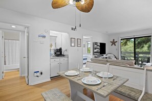 Uma cozinha moderna com armários brancos, um espaço de jantar com mesa de madeira posta para quatro pessoas e uma grande janela com vista para o exterior.