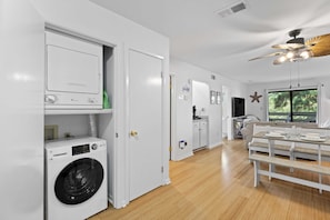 A modern kitchen with a built-in washer and dryer, a dining area with a bench, and a ceiling fan. - Fiddler's Cove - 2 Pool -Tennis - Hot Tub - Gym - Walk to the Beach! (Hilton Head Island)