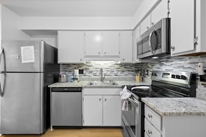 A modern kitchen with stainless steel appliances, white cabinets, a granite countertop, and a tiled backsplash. - Fiddler's Cove - 2 Pool -Tennis - Hot Tub - Gym - Walk to the Beach! (Hilton Head Island)