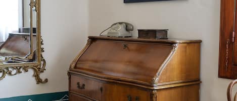 A wooden chest of drawers with a telephone on top, a mirror with ornate frame, and a framed picture on the wall.