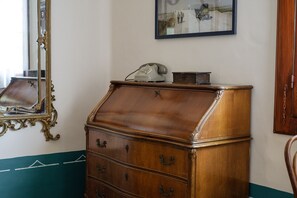 Une commode en bois sur laquelle est posé un téléphone, un miroir avec un cadre orné et un tableau encadré accroché au mur.