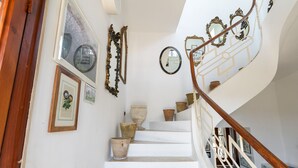 Una scala con gradini bianchi, una ringhiera in legno e diversi elementi decorativi tra cui quadri e specchi.