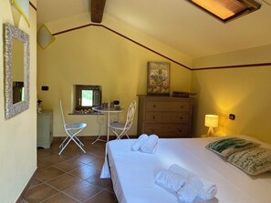 A bedroom with a bed, two chairs, a dresser, a window, and a painting on the wall.