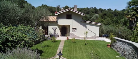 Casa de una planta con base de piedra, techo de tejas y entrada con camino pavimentado.