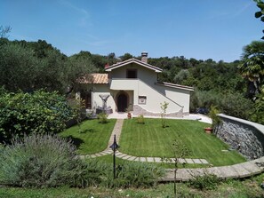 A single-story house with a stone foundation, a tiled roof, and a paved driveway leading to the entrance.