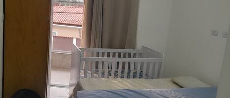 Un dormitorio con una cama, una cuna, un radiador y una puerta que da a un espacio exterior.