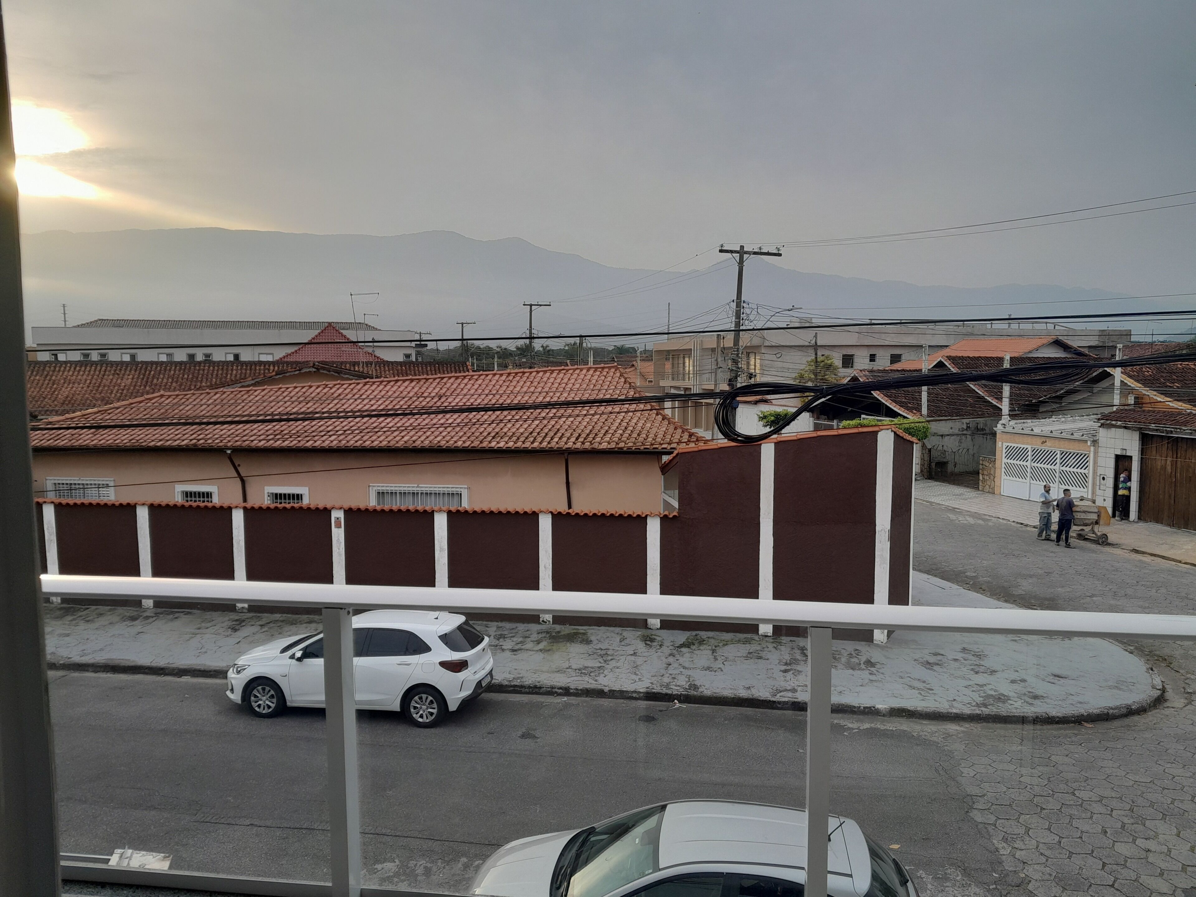 A residential street with houses, a white car, and a clear view of distant mountains.