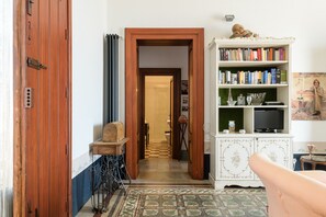 Une pièce avec une porte en bois, un radiateur, une bibliothèque, un téléviseur et un tapis à motifs.