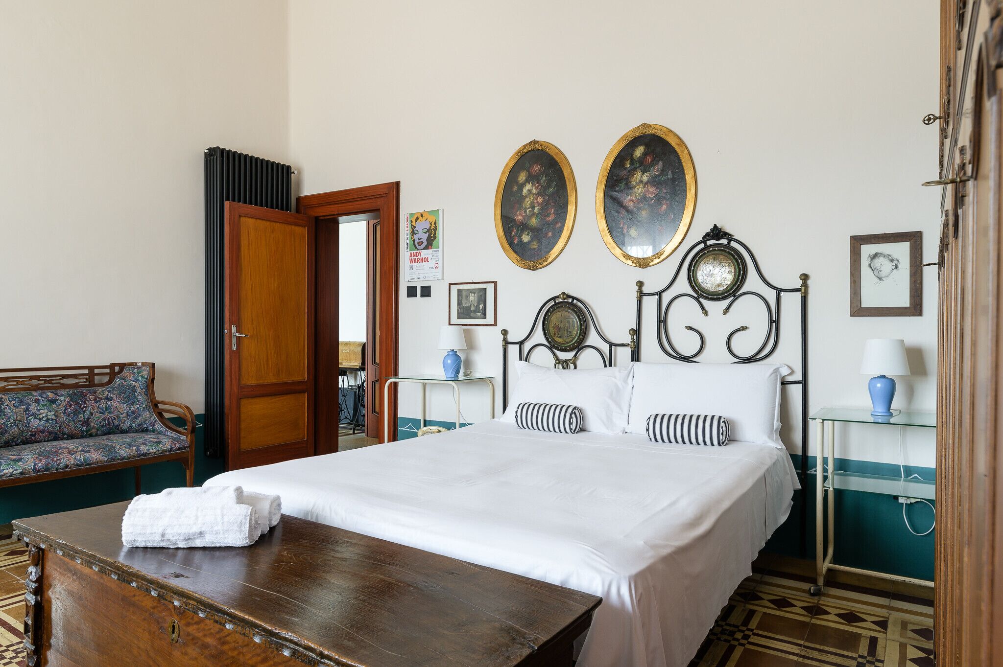 A hotel room with a bed, a wooden chest, a sofa, and two wall-mounted mirrors.