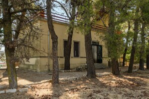 Un bâtiment à la façade jaune, entouré d’arbres et bordé d’un sol aride.