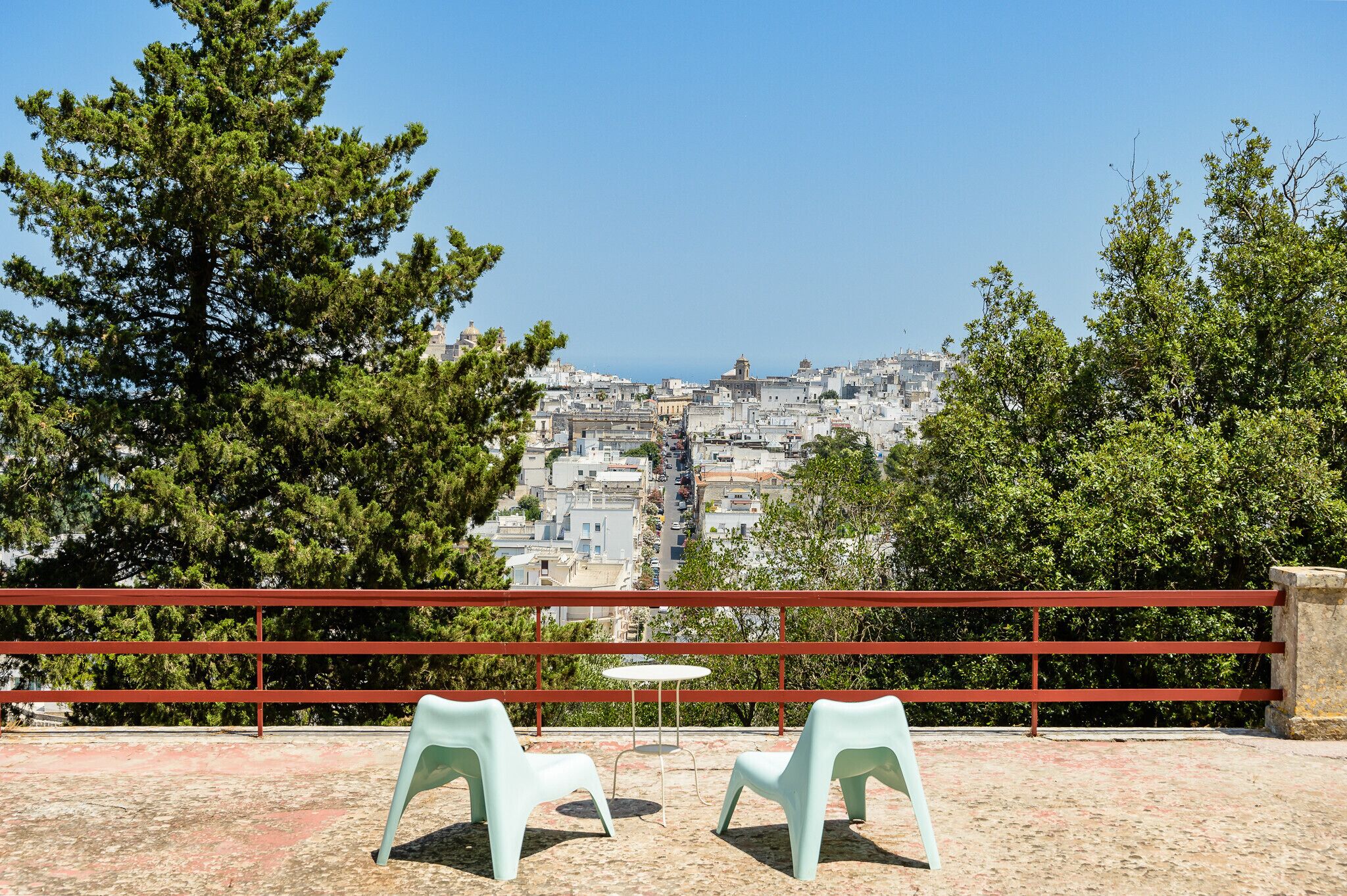 Eine Terrasse mit zwei Stühlen und einem Tisch, mit Blick auf eine dicht bebauten Stadtlandschaft aus Gebäuden und Bäumen.