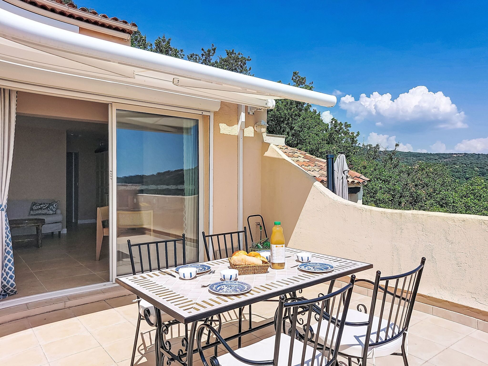 A patio with a table set for two, a bottle of orange juice, and a basket of bread.