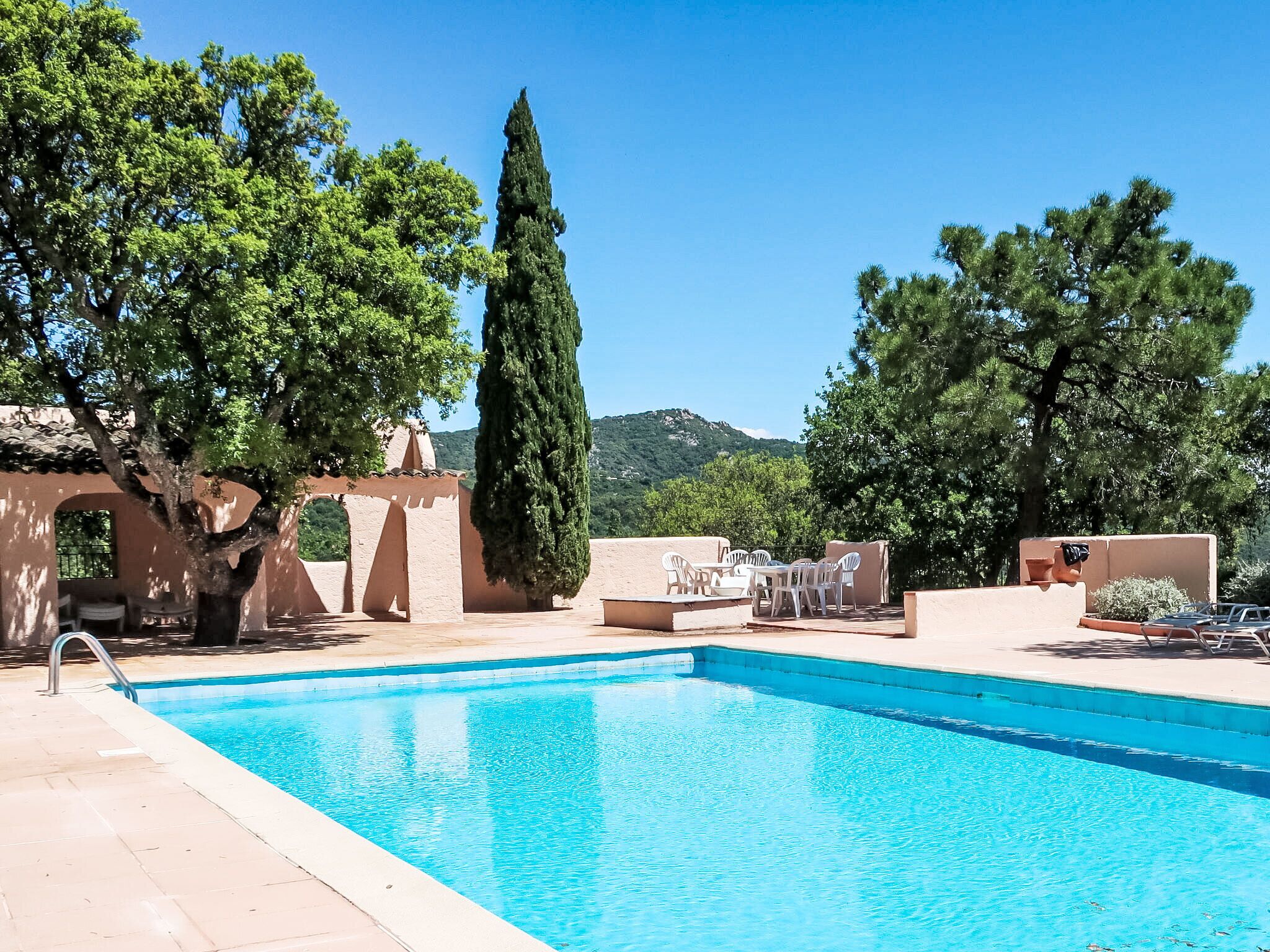 A swimming pool with a clear blue water, surrounded by trees and a mountain in the background.