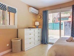 Ein Schlafzimmer mit einem Bett, einem Schminktisch, einer Klimaanlage und einem Fenster mit gemusterten Vorhängen.