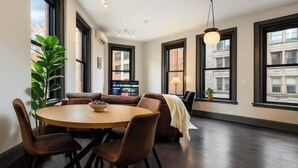Uma sala de estar moderna com uma mesa redonda, assentos confortáveis, janelas amplas e um lustre.