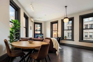 Ein stilvolles Wohnzimmer mit rundem Tisch, gemütlicher Sitzgelegenheit, großen Fenstern und einer Pendelleuchte.