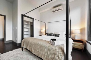 Ein modernes Schlafzimmer mit Himmelbett, begehbarem Kleiderschrank und Nachttisch mit Lampe.