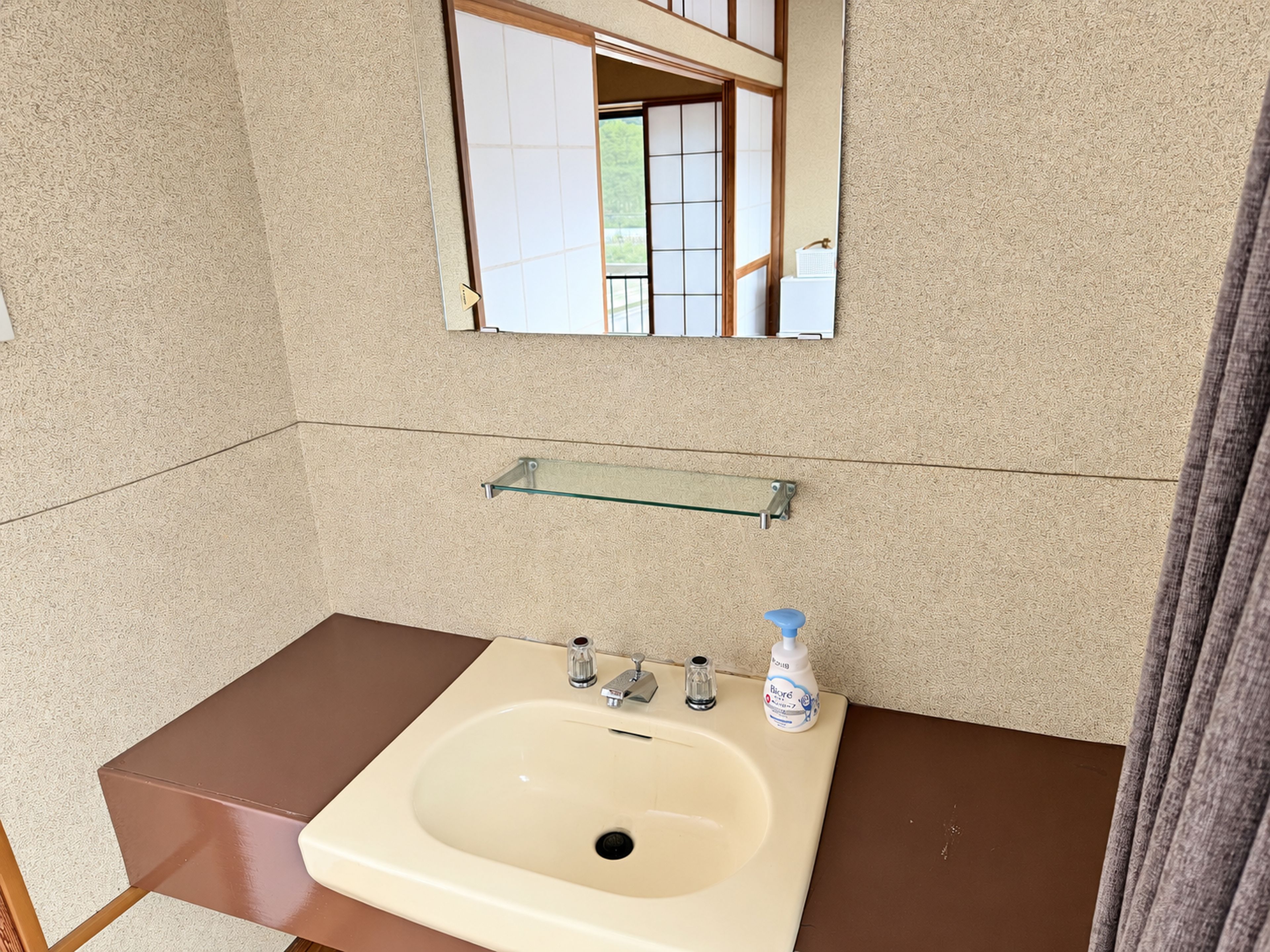 A bathroom with a beige sink, a mirror above it, and a glass shelf below.