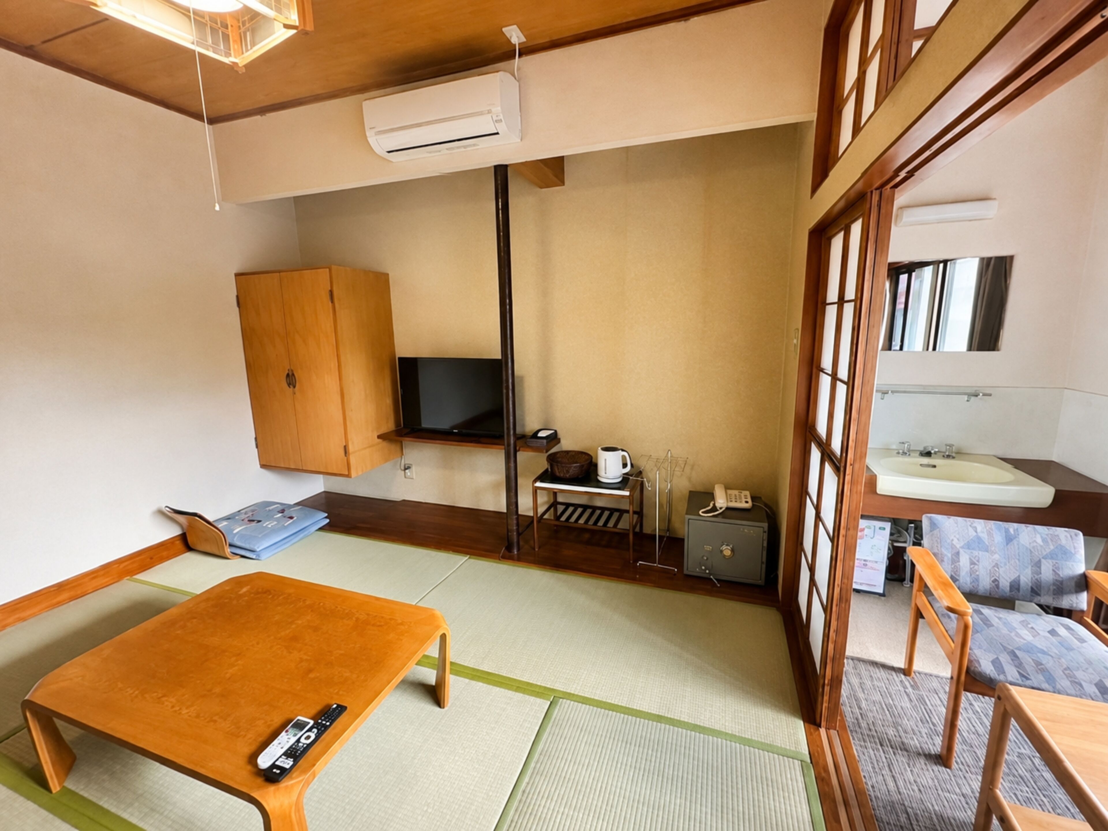 A traditional Japanese-style room with tatami flooring, a wooden table, a television, a cabinet, and a small kitchenette area.