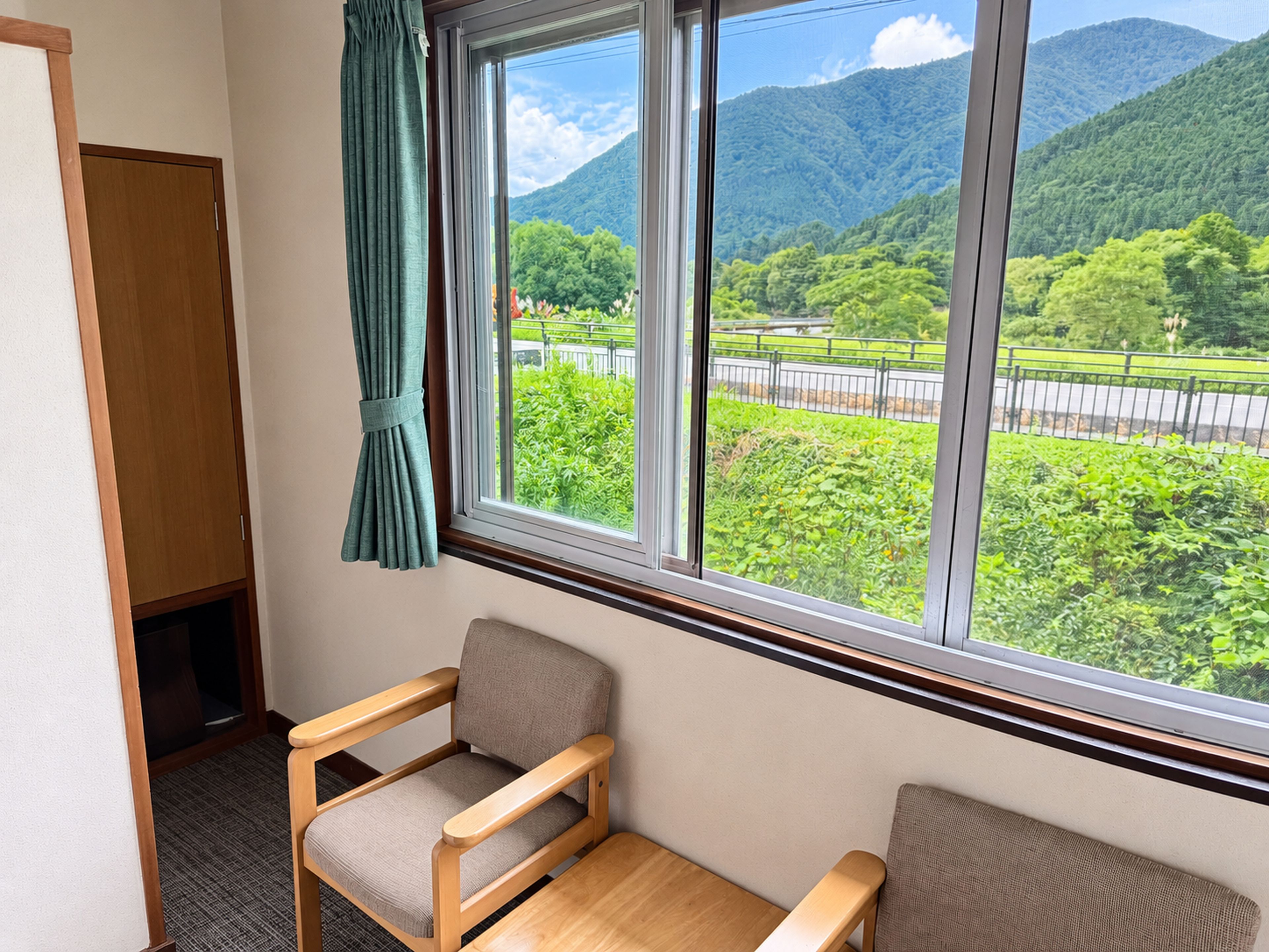 Una habitación con vista a un paisaje montañoso a través de una ventana, una silla de madera y una pequeña mesa.