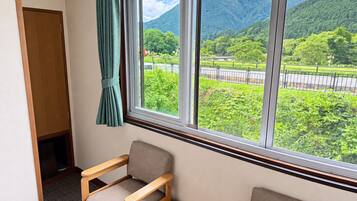Una habitación con vista a un paisaje montañoso a través de una ventana, una silla de madera y una pequeña mesa.