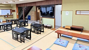 A traditional tatami mat room with tables and benches, a television, and a staircase.