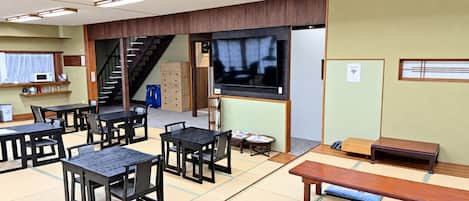 A traditional tatami mat room with tables and benches, a television, and a staircase.