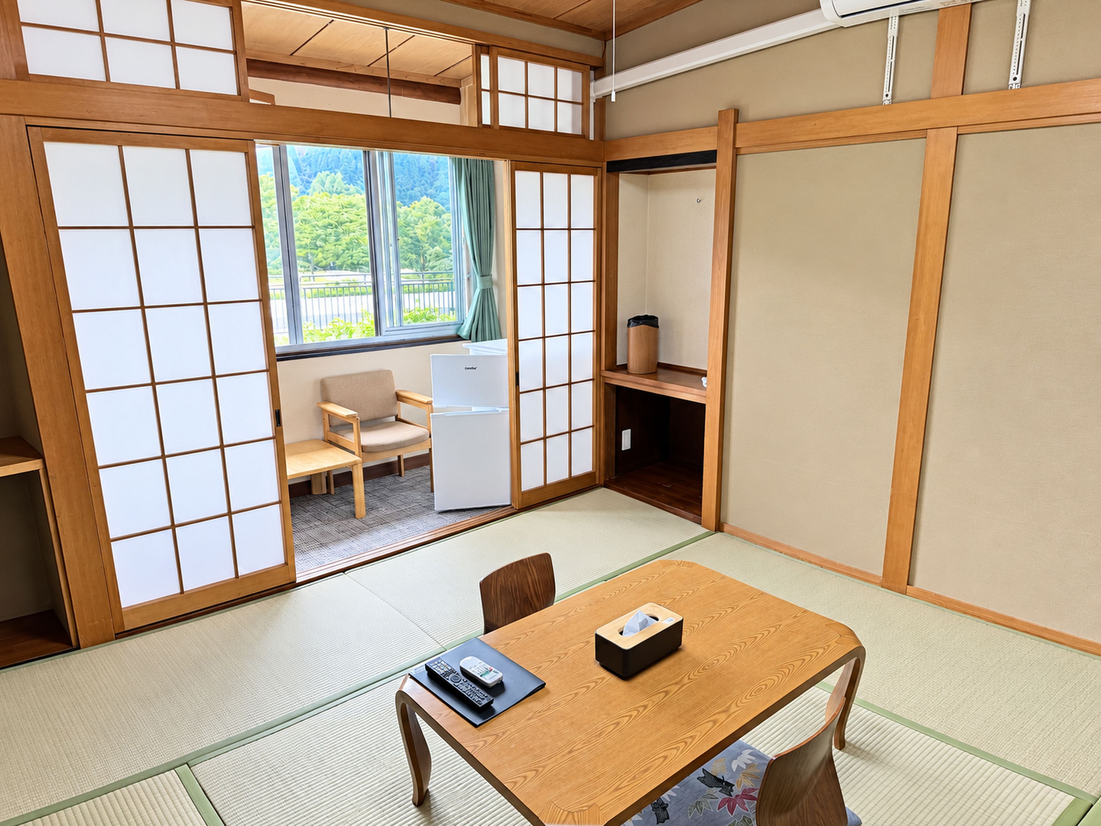 Una habitación japonesa tradicional con suelo de tatami, una mesa baja, una silla, un refrigerador y puertas correderas.