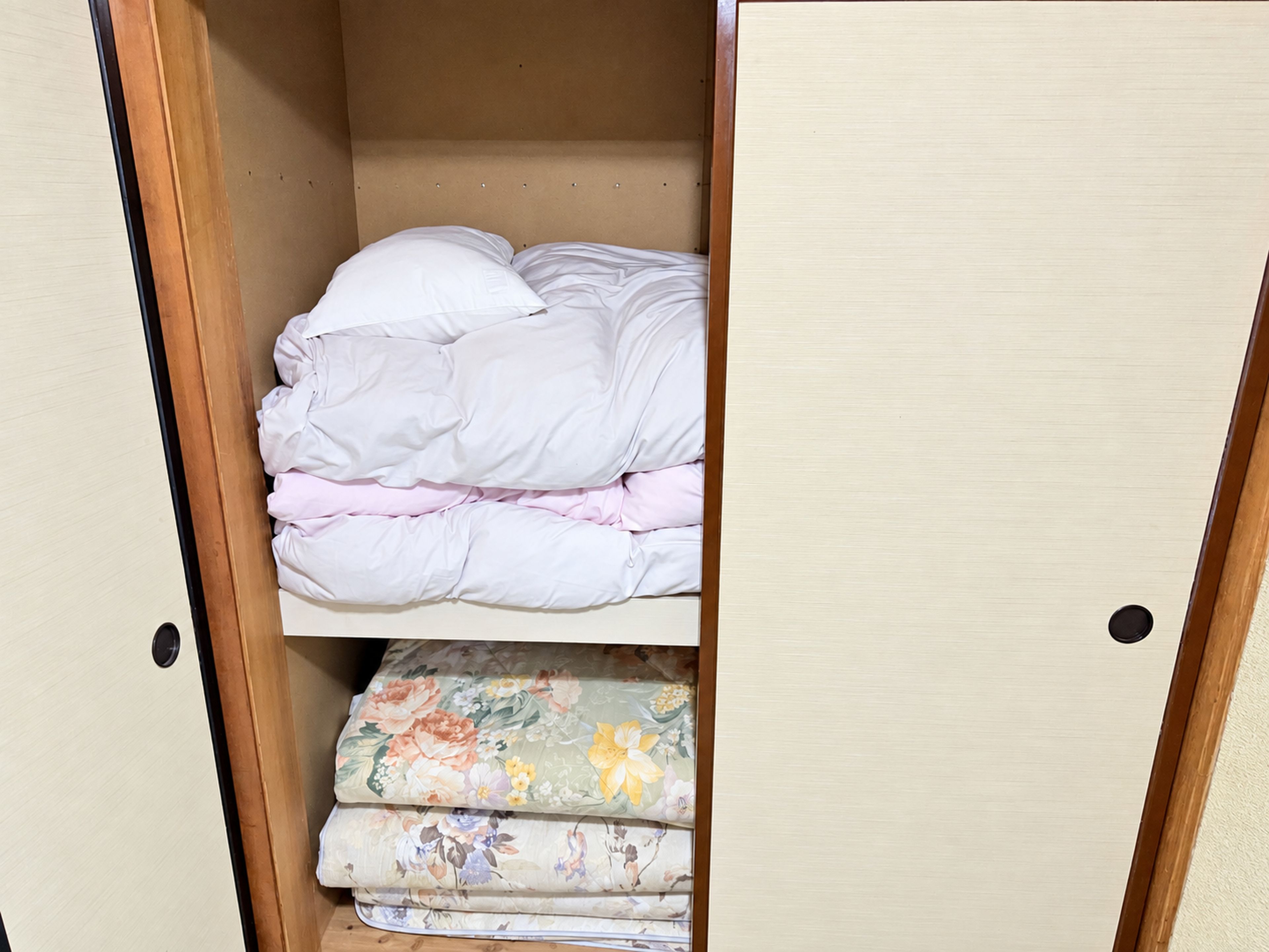 A wardrobe with a bed at the bottom and a shelf above with folded bedding.