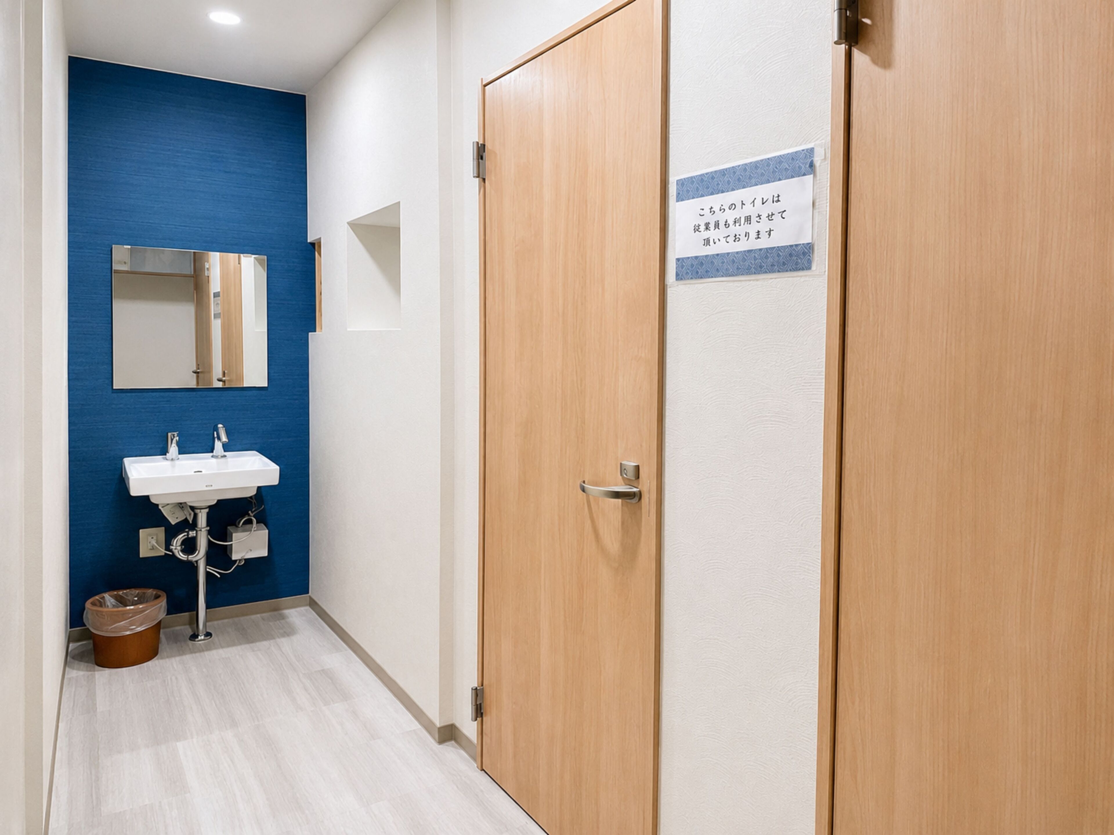 Un pasillo con pared azul, un lavamanos blanco y una puerta de madera con un cartel.