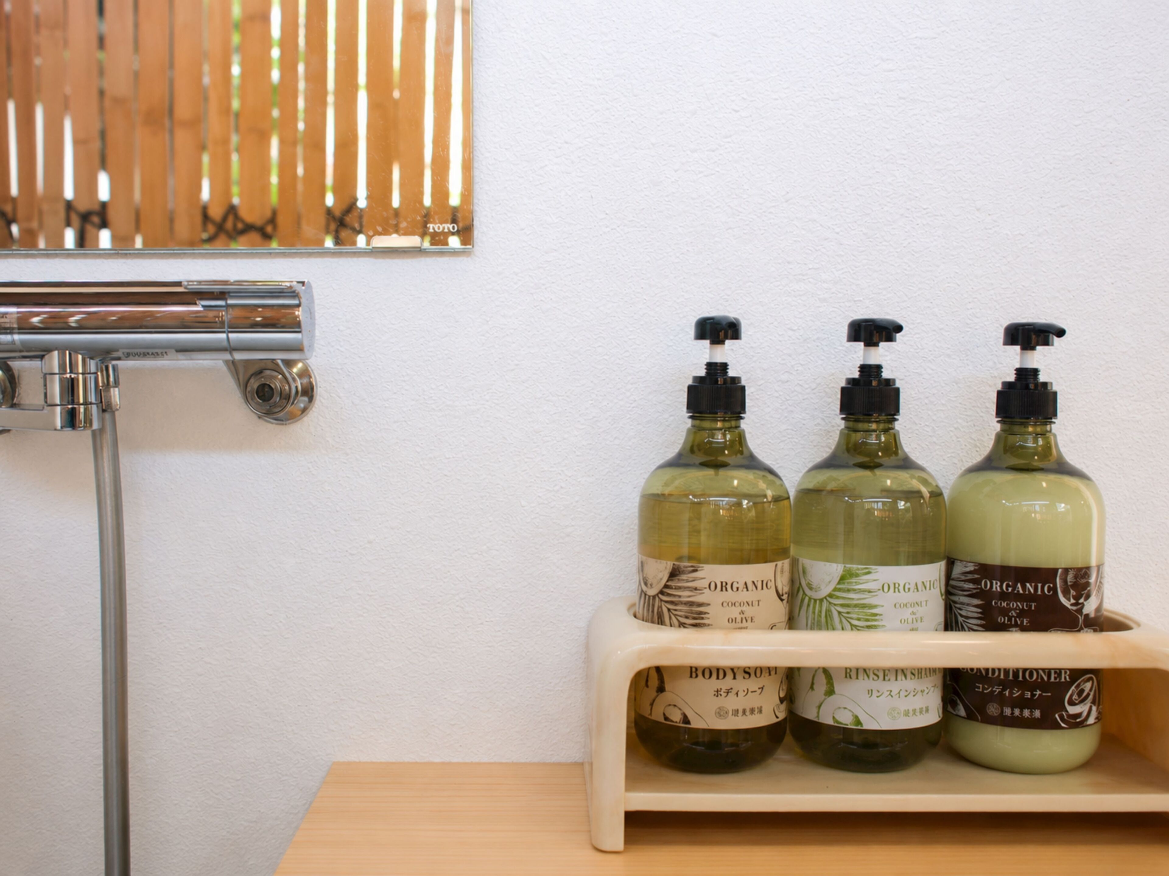 Et badeværelse med en træhylde, der indeholder tre flasker økologisk kokosolie-badyolie og conditioner.