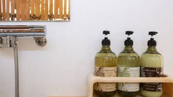 Et badeværelse med en træhylde, der indeholder tre flasker økologisk kokosolie-badyolie og conditioner.