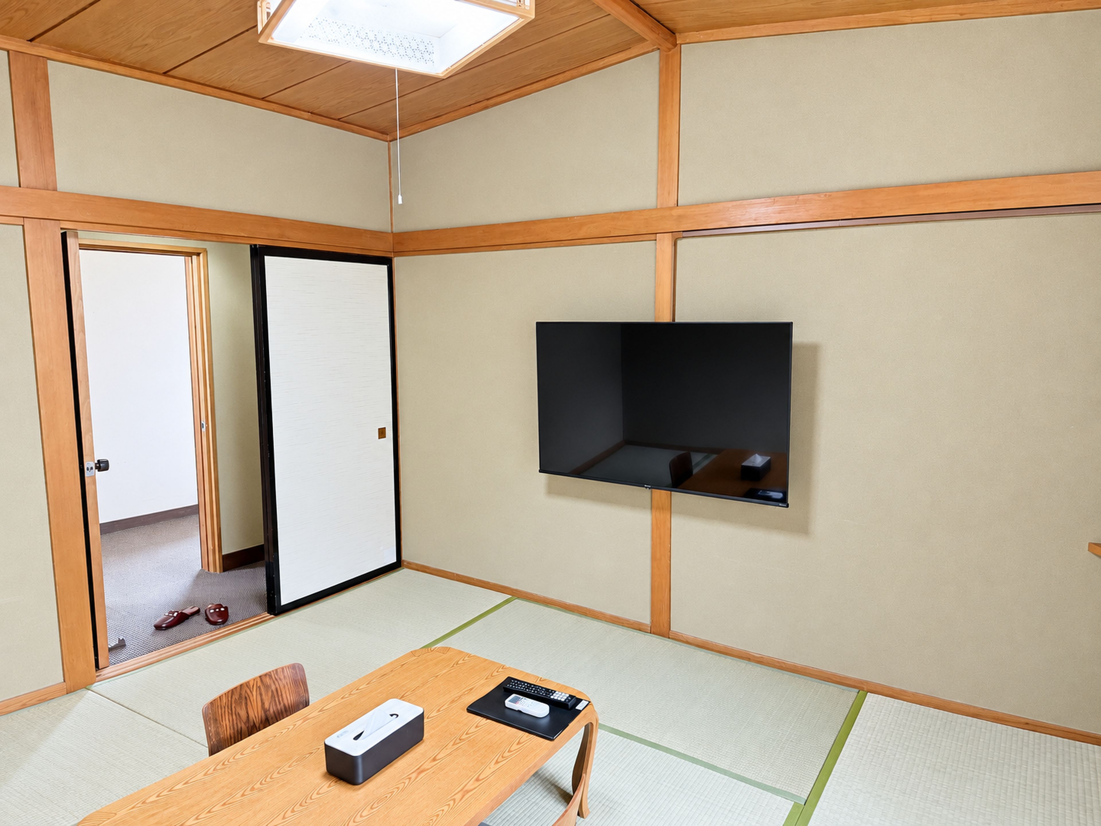 A room with tatami flooring, a sliding door, a television mounted on the wall, and a table with a remote control and a box.