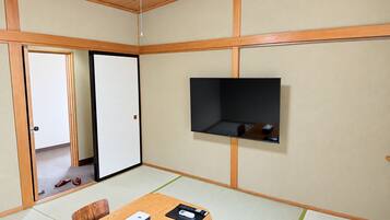 A room with tatami flooring, a sliding door, a television mounted on the wall, and a table with a remote control and a box.