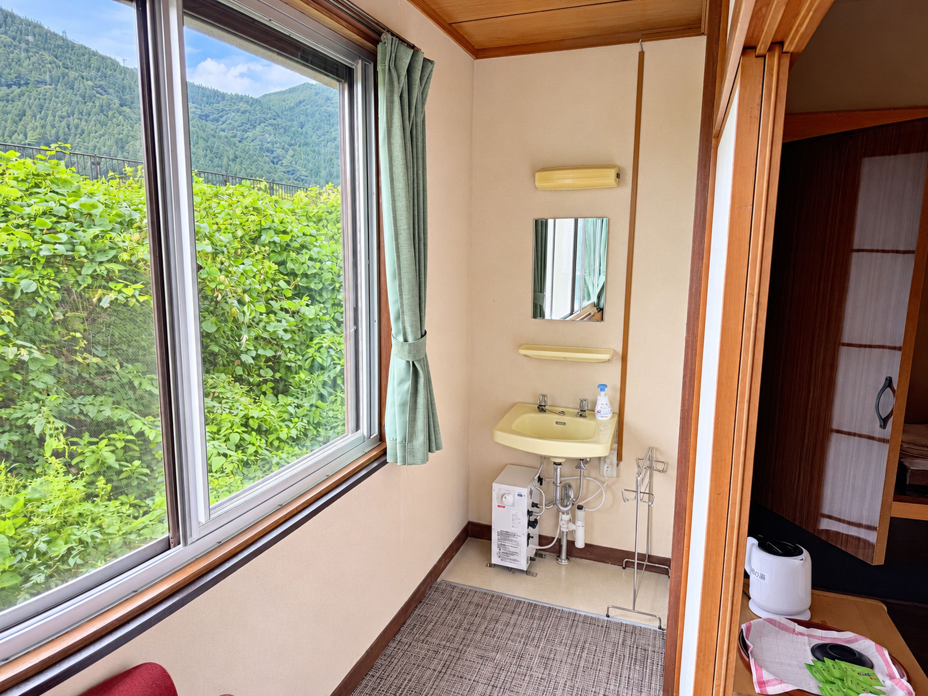 A bathroom with a window, sink, mirror, and a small heater.