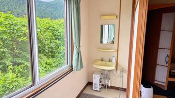 A bathroom with a window, sink, mirror, and a small heater.