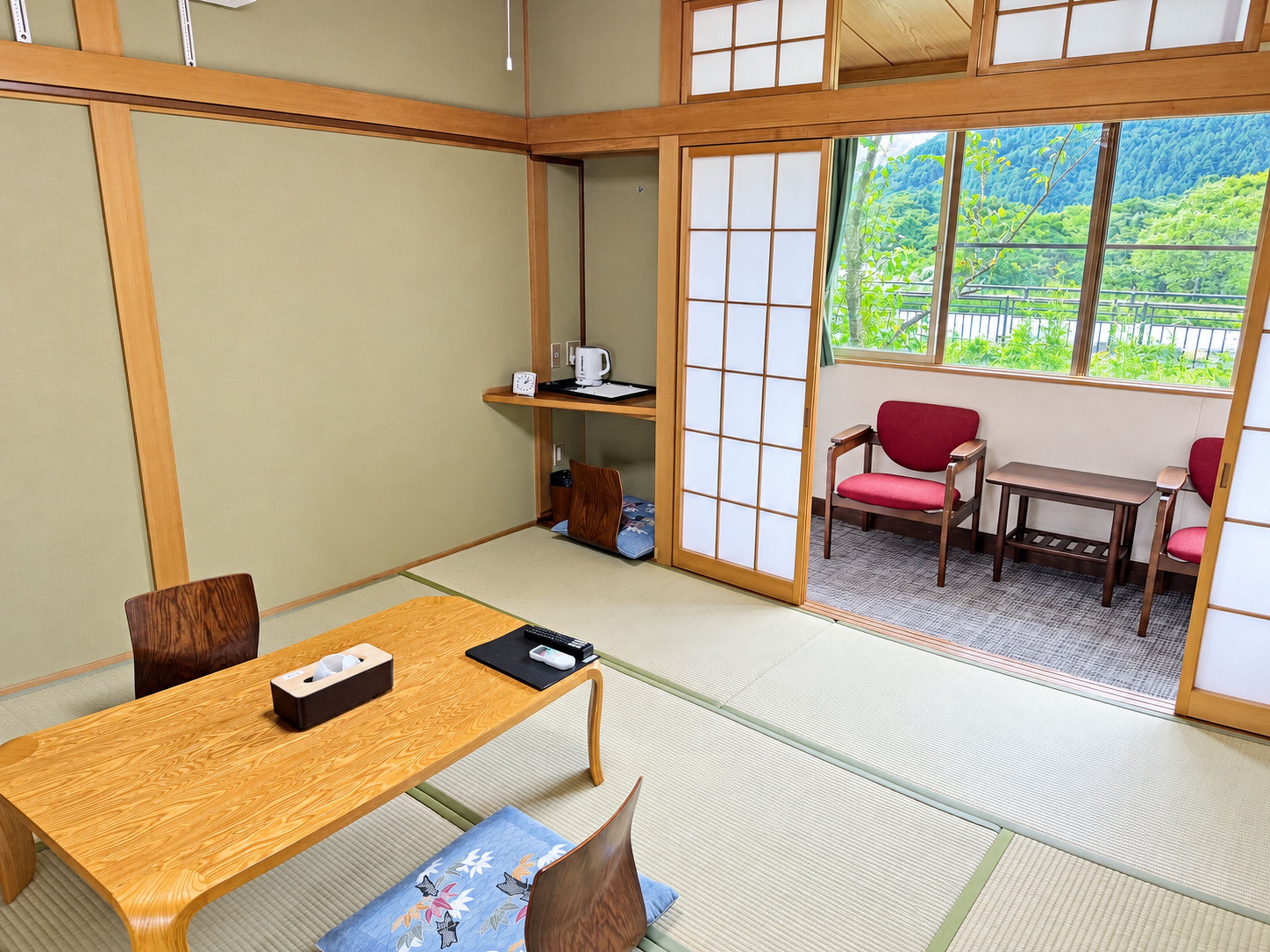 A traditional Japanese room with tatami flooring, a low wooden table, and a sliding door leading to a balcony with a view of greenery.