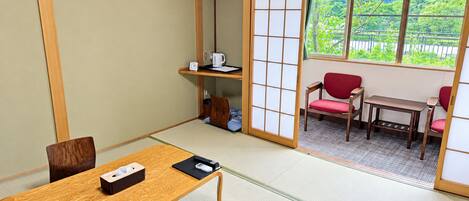 A traditional Japanese room with tatami flooring, a low wooden table, and a sliding door leading to a balcony with a view of greenery.