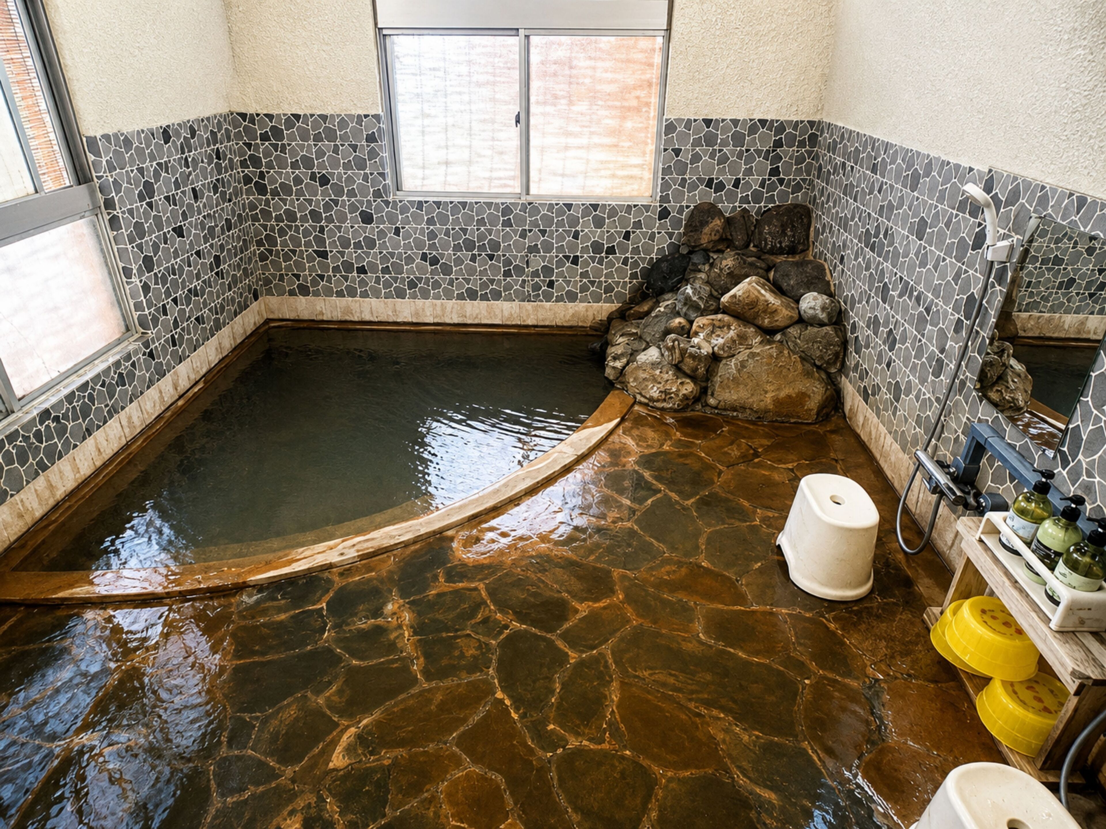 Un jacuzzi con suelo de piedra, borde de madera, pared de piedra y ventana.