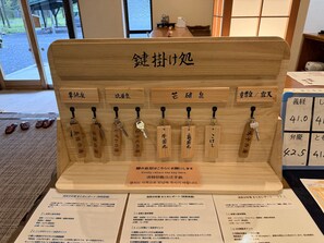 Un expositor de llaves de madera con etiquetas en japonés, un cartel solicitando la devolución de las llaves y un menú con texto en japonés.