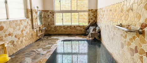A spa room with a stone wall, a window, and a bathtub.