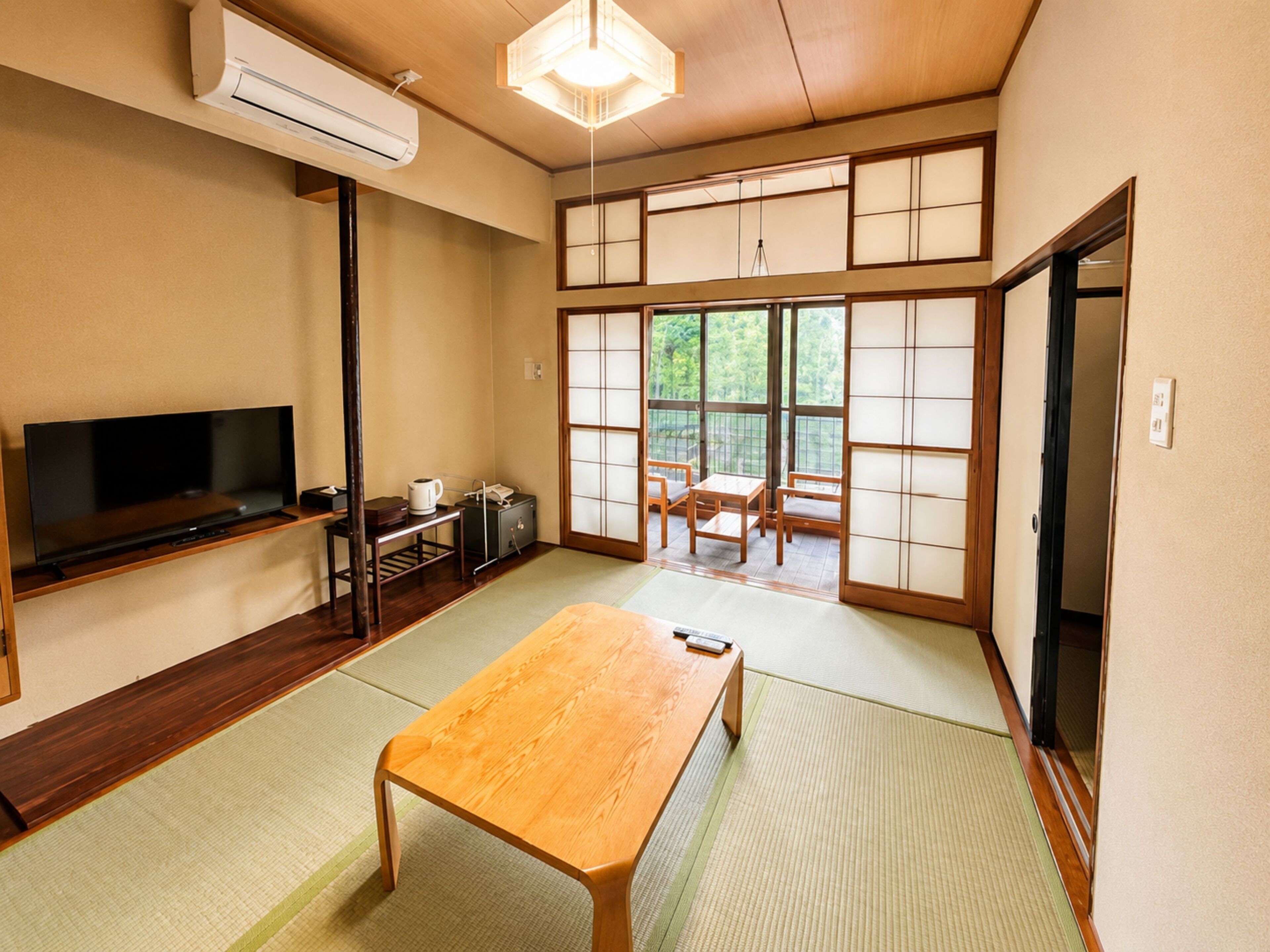 Een traditionele Japanse kamer met tatami vloeren, een televisie, een tafel en schuifdeuren die uitkomen op een balkon.
