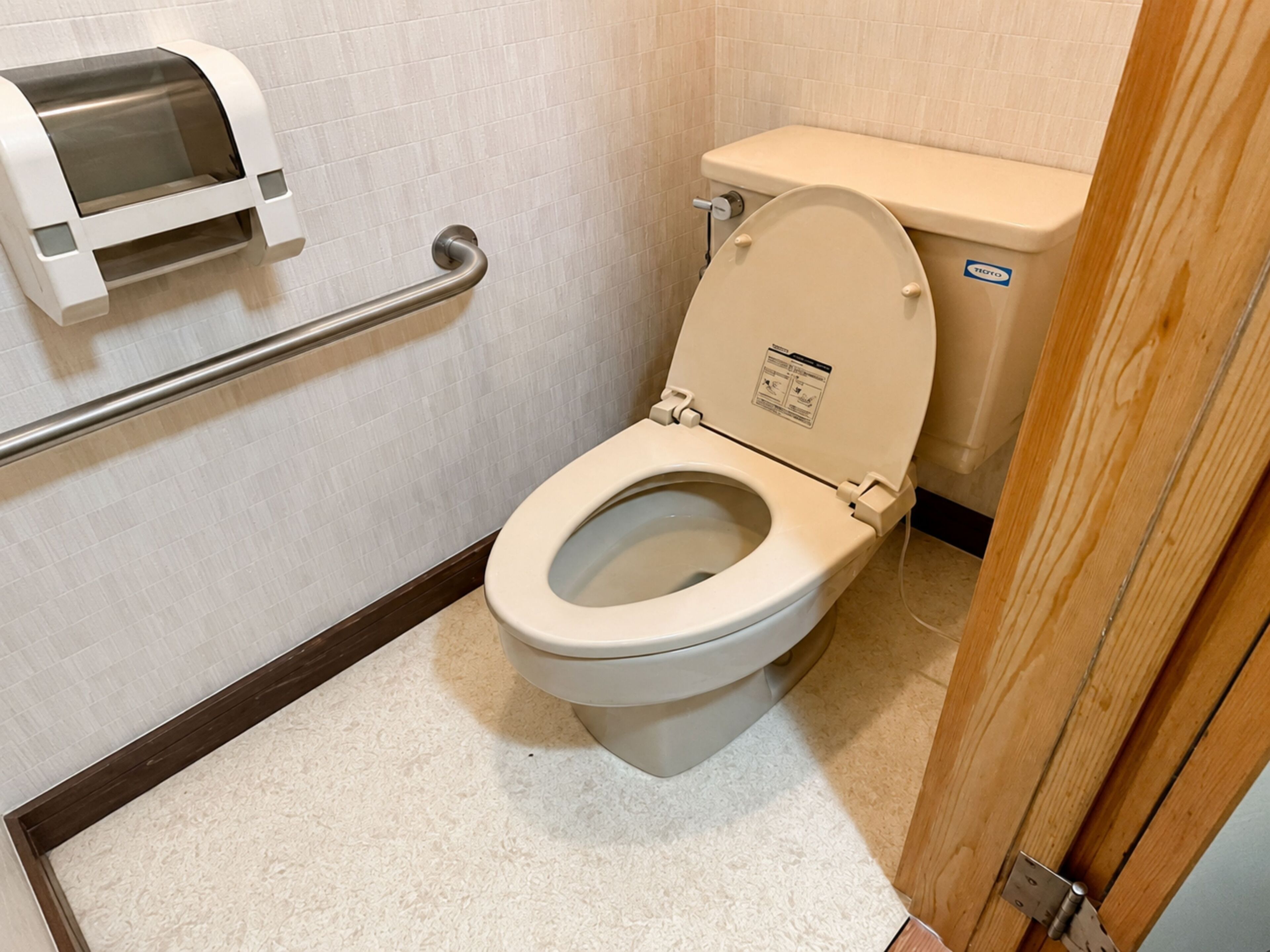 A toilet with a raised seat, a handrail, and a paper towel dispenser.